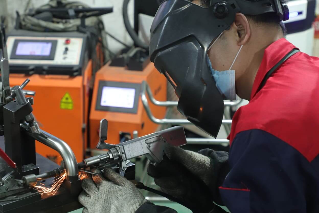 Worker performing manual laser welding on metal tube at Yizhijie hardware factory workstation